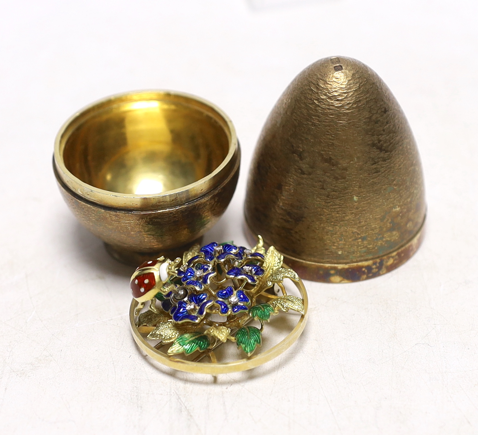 An Elizabeth II silver gilt surprise egg, in the manner of Stuart Devlin, maker possibly Algernon Asprey?, opening to reveal an enamelled and diamond set scene of a ladybird upon a flower, London, 1973, 79mm.